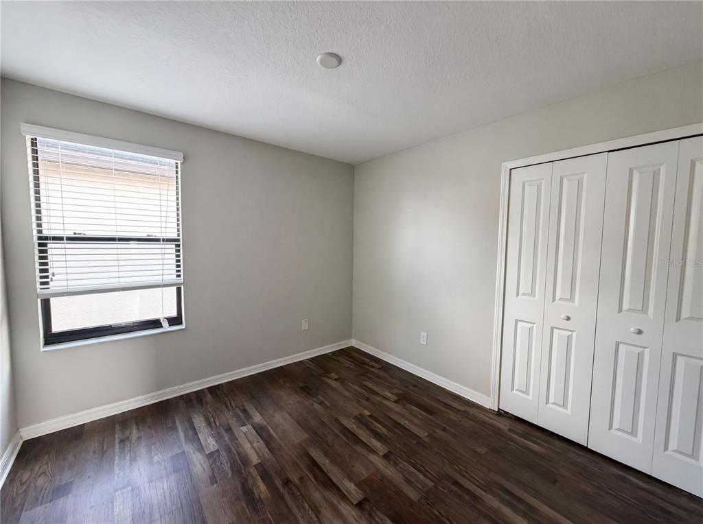 An empty bedroom features light gray walls, dark wood-look flooring, a window, and white closet doors — 11126 HUDSON HILLS LANE, RIVERVIEW, FL