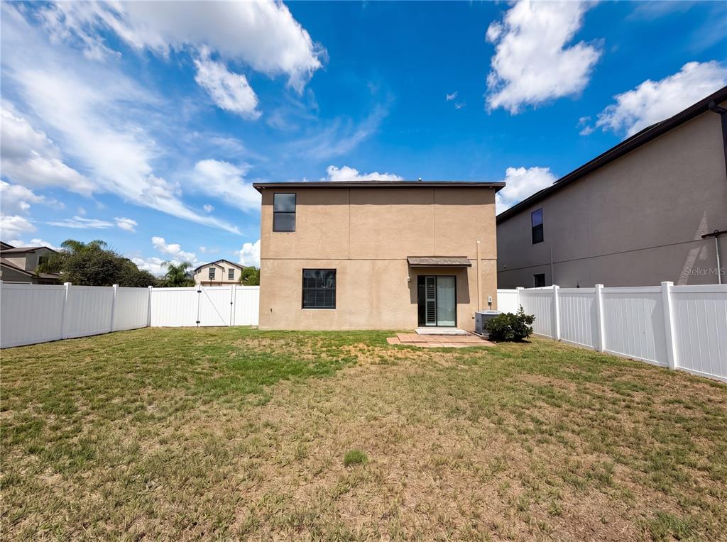The backyard of a two-story house features a tan stucco exterior, a sliding glass door, and white vinyl fencing — 11126 HUDSON HILLS LANE, RIVERVIEW, FL