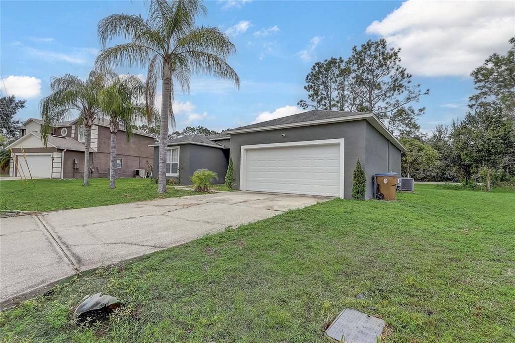 A gray single-story house features a white garage door, a concrete driveway, and palm trees — 1023 EMBRUN COURT, KISSIMMEE, FL