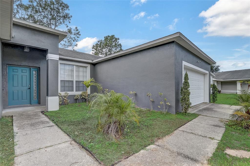 A gray stucco house features a teal front door, a garage, and a front lawn — 1023 EMBRUN COURT, KISSIMMEE, FL