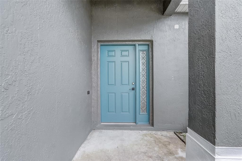 A blue front door with a side light is set into a gray stucco entryway — 1023 EMBRUN COURT, KISSIMMEE, FL