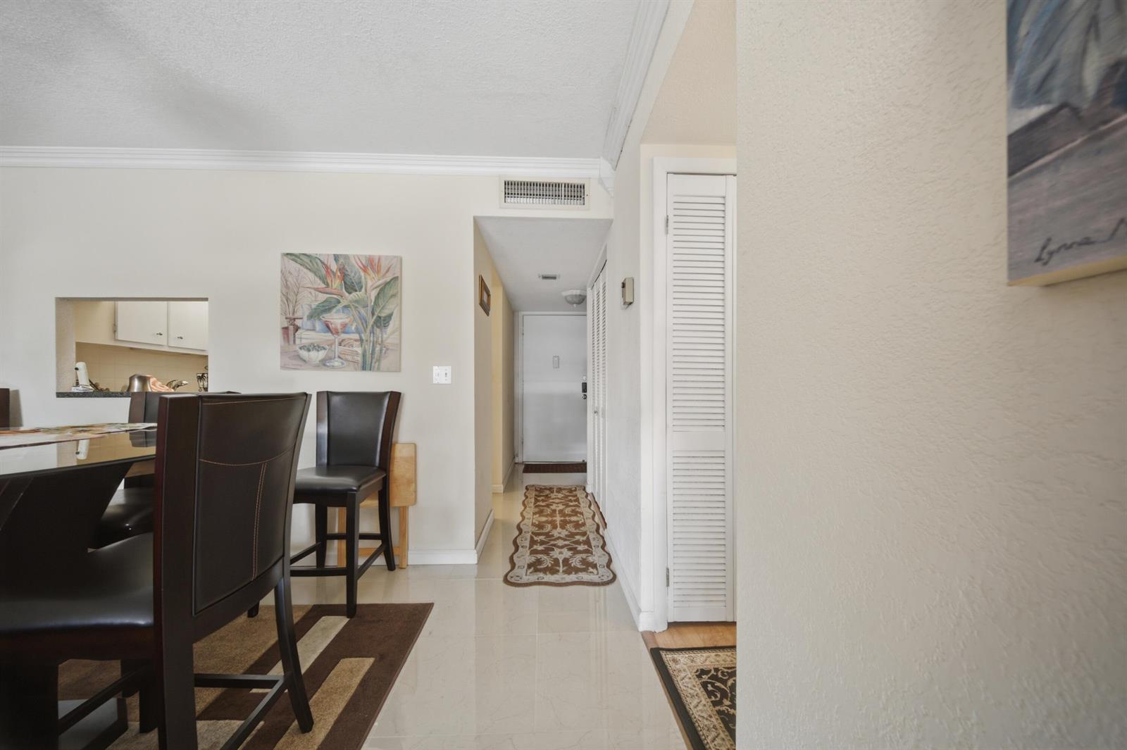 A dining area with dark chairs leads to a hallway with a white door — 3040 Holiday Springs Boulevard # 212, Margate FL 33063, MARGATE, FL