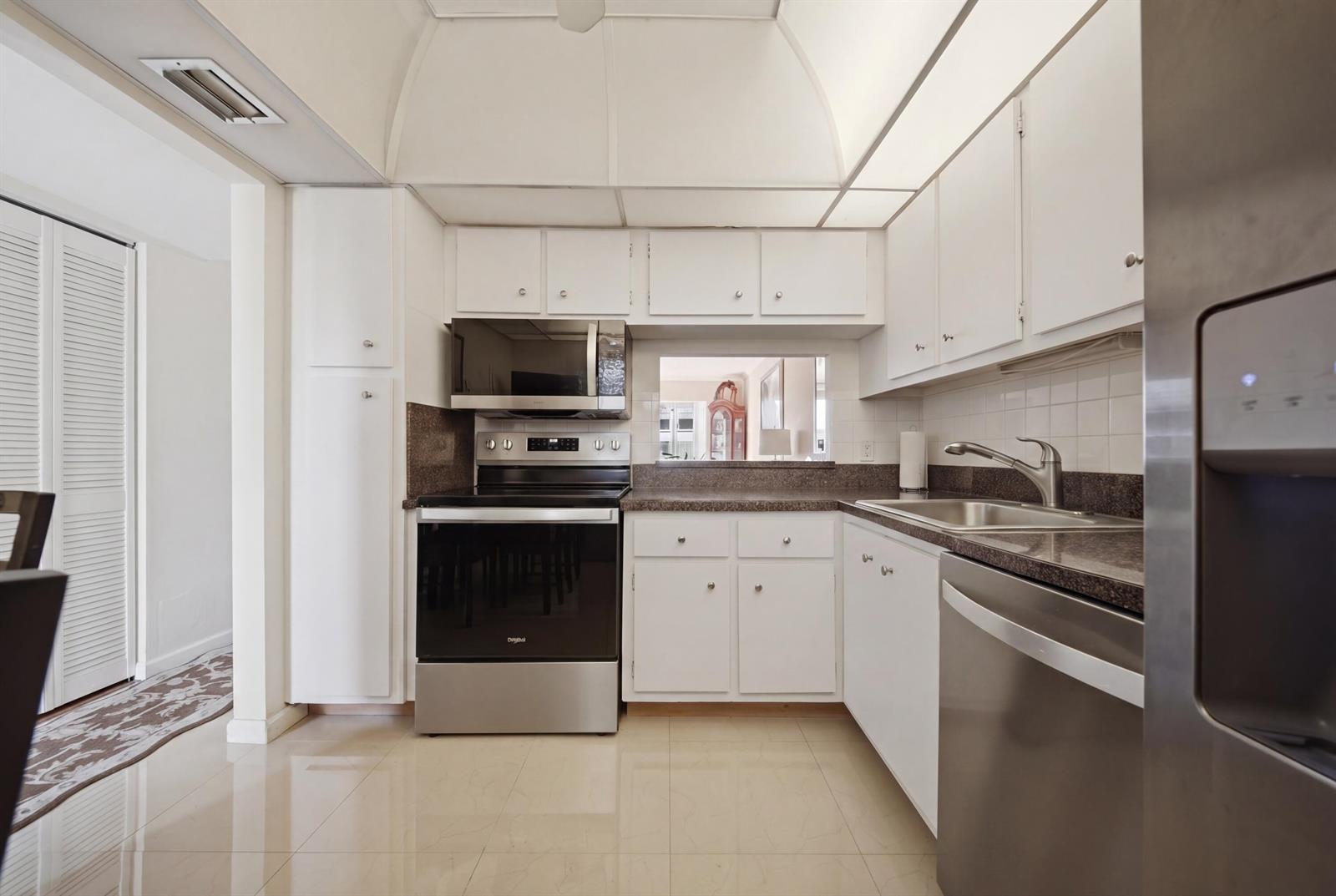A kitchen with white cabinets, stainless steel appliances, dark countertops, and light tile flooring — 3040 Holiday Springs Boulevard # 212, Margate FL 33063, MARGATE, FL