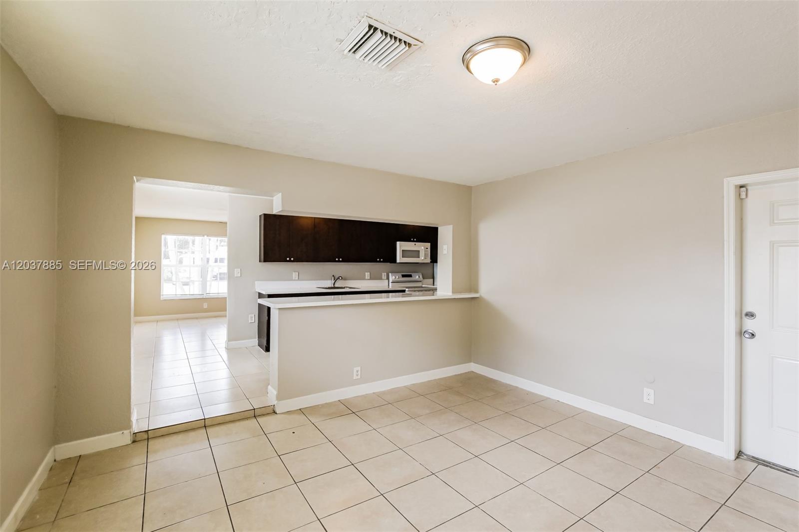 An open-concept kitchen with dark cabinets and a breakfast bar overlooks a tiled dining area — 5980 NW 24th Ct, Margate FL 33063, MARGATE, FL
