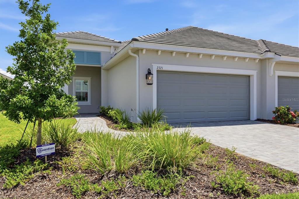 A beige single-story house exterior features a gray garage door, tile roof, and paved driveway — 2321 BLUE MAHOE LANE, SARASOTA, FL