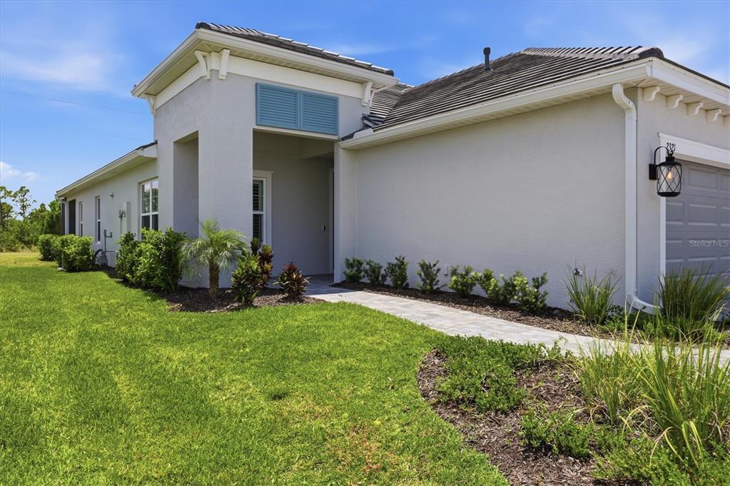 A light-colored house exterior features a covered entryway, a paved walkway, and a garage — 2321 BLUE MAHOE LANE, SARASOTA, FL