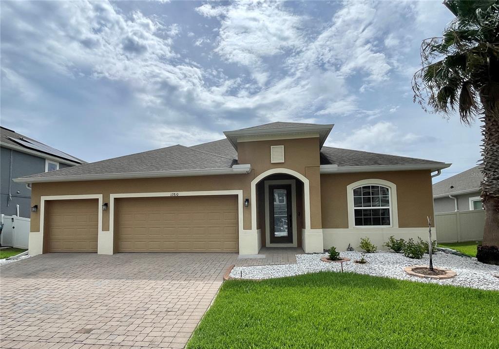 A single-story house with a tan stucco exterior, a three-car garage, and a paved driveway — 12810 BOGGY VIEW DR, ORLANDO, FL