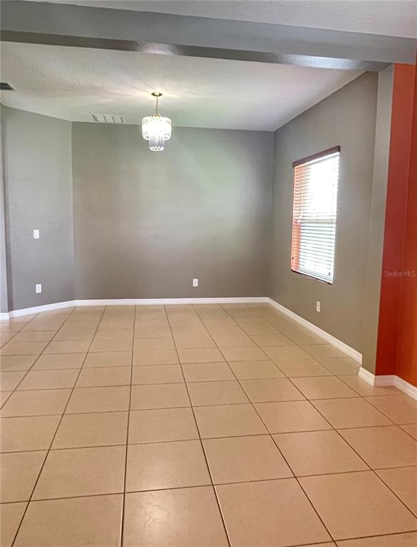 An empty dining room features beige tile flooring, gray walls, and a hanging chandelier — 12810 BOGGY VIEW DR, ORLANDO, FL