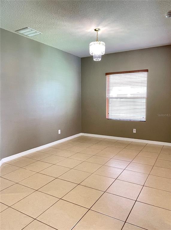 An empty room features beige tile flooring, two-toned walls, a window with blinds, and a chandelier — 12810 BOGGY VIEW DR, ORLANDO, FL