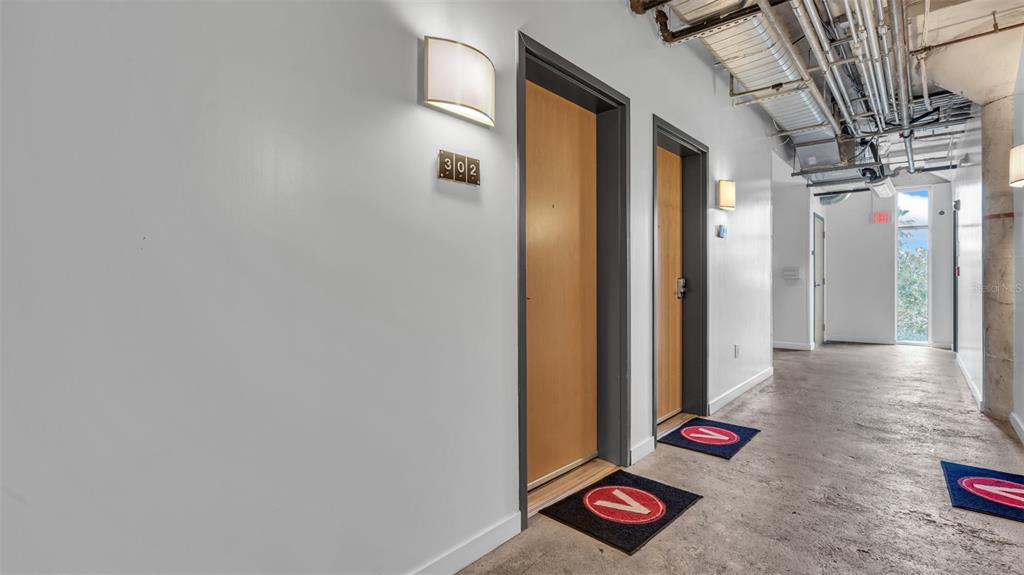 A hallway with two wooden doors, concrete floors, and exposed industrial ceiling pipes — 101 N 12TH STREET UNIT 302, TAMPA, FL