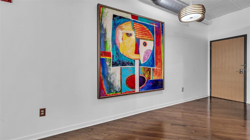A room with hardwood floors, a large abstract painting on the wall, and a wooden door — 101 N 12TH STREET UNIT 302, TAMPA, FL