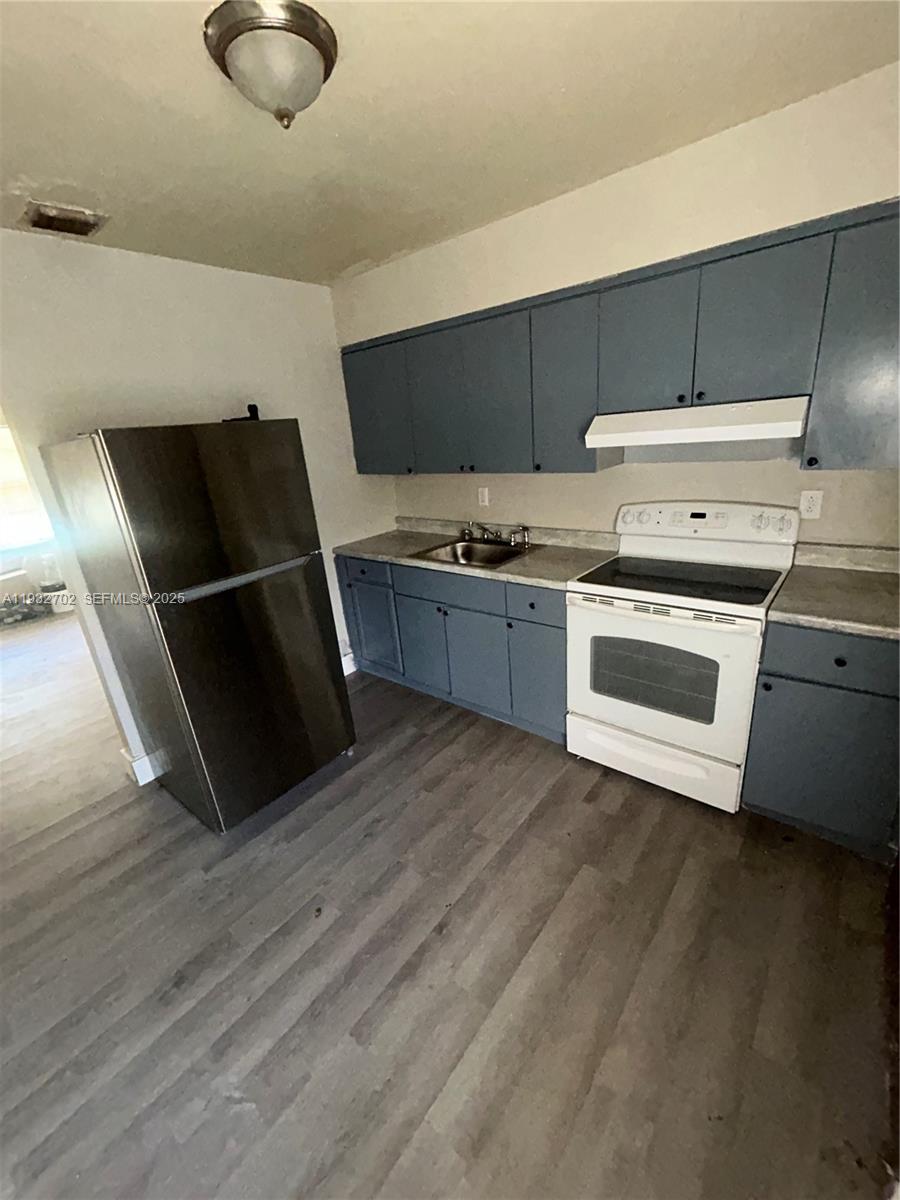 A kitchen features blue cabinets, a stainless steel refrigerator, and a white electric range — 1180 NW 64th St # B, Miami FL 33150, MIAMI, FL