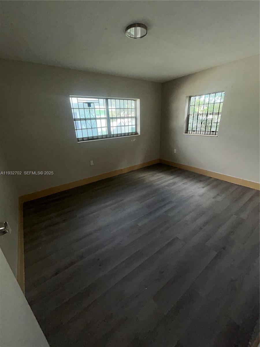 An empty bedroom features gray wood-look flooring, light walls, and two windows with security bars — 1180 NW 64th St # B, Miami FL 33150, MIAMI, FL
