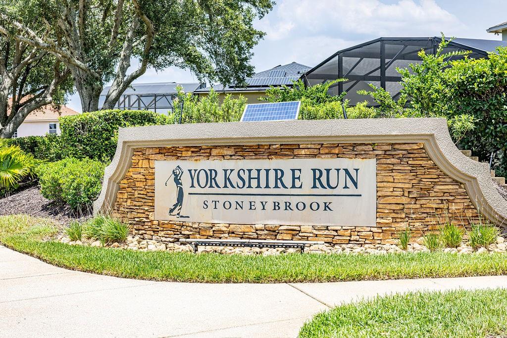 A stone monument sign for Yorkshire Run at Stoney Brook stands near a paved walkway — 14733 HARTFORD RUN DRIVE, ORLANDO, FL