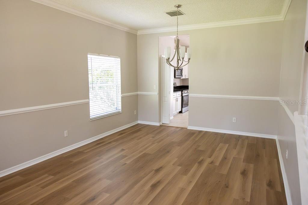 An empty dining room features light-colored walls, wood-look flooring, and a central chandelier — 14733 HARTFORD RUN DRIVE, ORLANDO, FL