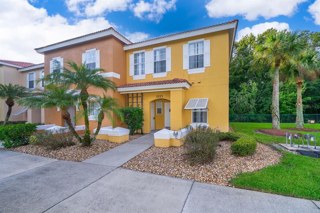 A two-story yellow stucco townhouse with a palm tree and a concrete walkway — 1113 PARK RIDGE CIRCLE, KISSIMMEE, FL