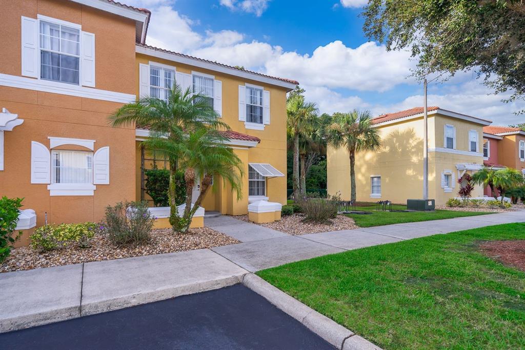 A two-story yellow stucco townhouse with a palm tree and a sidewalk in front — 1113 PARK RIDGE CIRCLE, KISSIMMEE, FL
