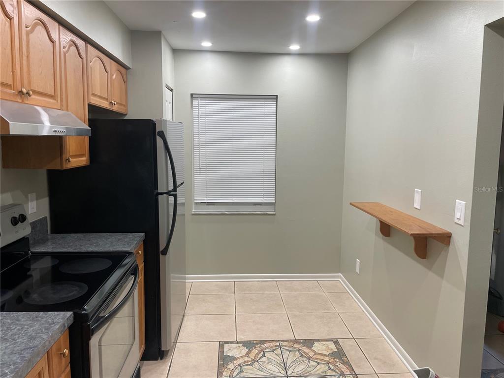 A kitchen features wood cabinets, a black refrigerator, a stove, and a wall-mounted shelf — 6366 71ST STREET N, PINELLAS PARK, FL