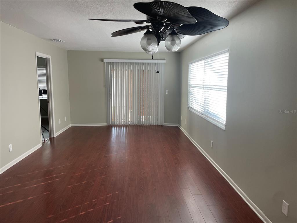 An empty room features dark wood-look flooring, light gray walls, a ceiling fan, and sliding doors — 6366 71ST STREET N, PINELLAS PARK, FL