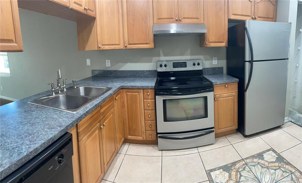 A kitchen features wood cabinets, a stainless steel stove, a refrigerator, and a double sink — 6366 71ST STREET N, PINELLAS PARK, FL