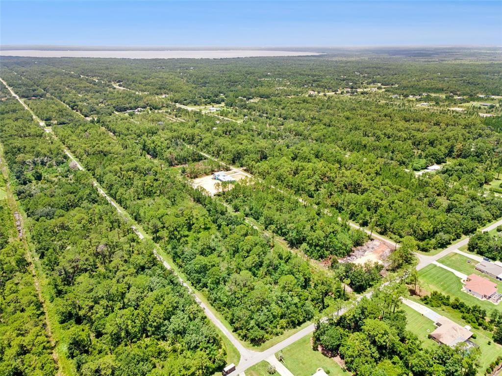 An aerial view shows a wooded residential area with scattered houses and a distant lake — 0 PANDORA DR, INDIAN LAKE ESTATES, FL