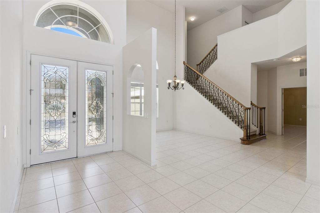 A bright foyer features white tile floors, a grand staircase, and a double front door — 3643 PEACEFUL VALLEY DRIVE, CLERMONT, FL