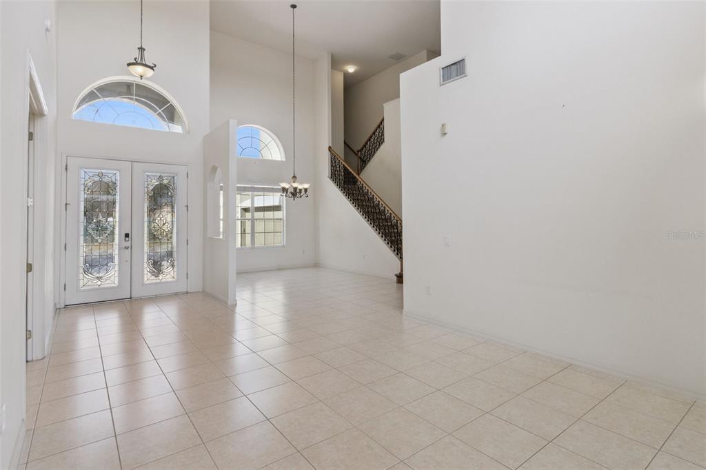 A bright, tiled entryway features a high ceiling, a staircase, and double glass-paneled doors — 3643 PEACEFUL VALLEY DRIVE, CLERMONT, FL