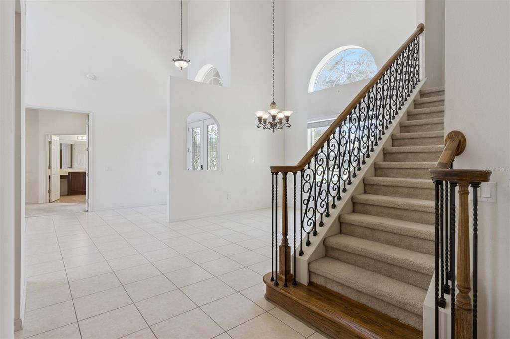 A foyer with tiled floors features a carpeted staircase with a decorative iron railing — 3643 PEACEFUL VALLEY DRIVE, CLERMONT, FL