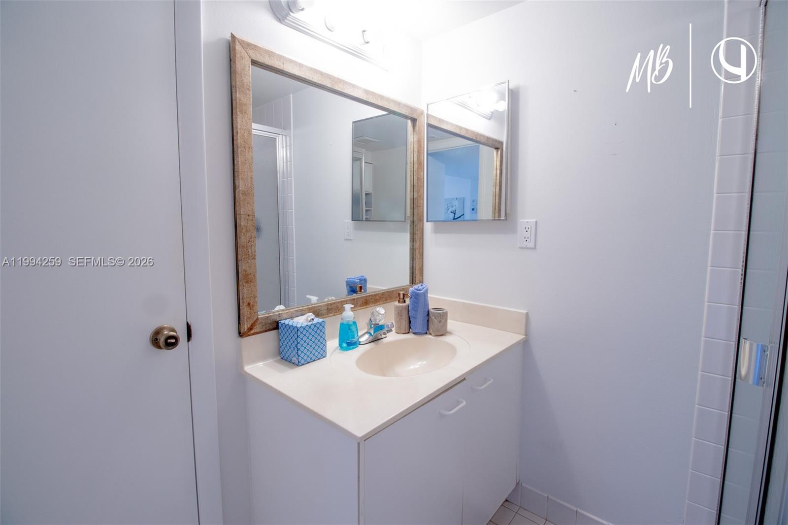 A bathroom features a white vanity with a beige countertop, a framed mirror, and a shower — SUNNY ISLES BEACH, FL