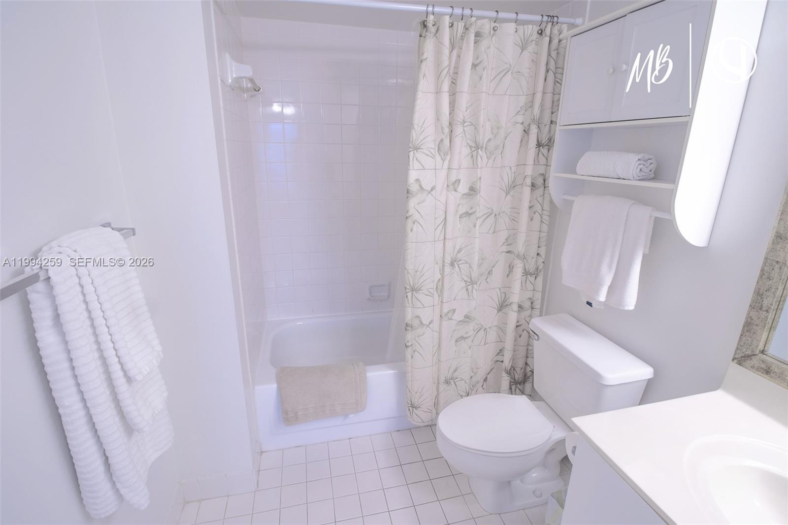 A bathroom features a white tiled tub-shower combo, a toilet, and a vanity cabinet — SUNNY ISLES BEACH, FL