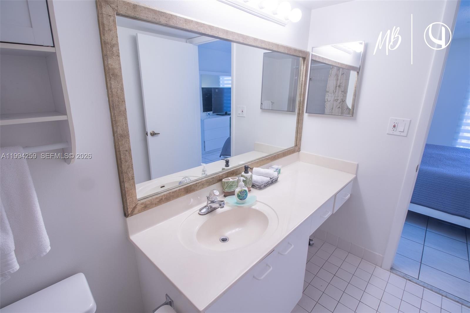 A bathroom features a white vanity, a large framed mirror, and white tile flooring — SUNNY ISLES BEACH, FL