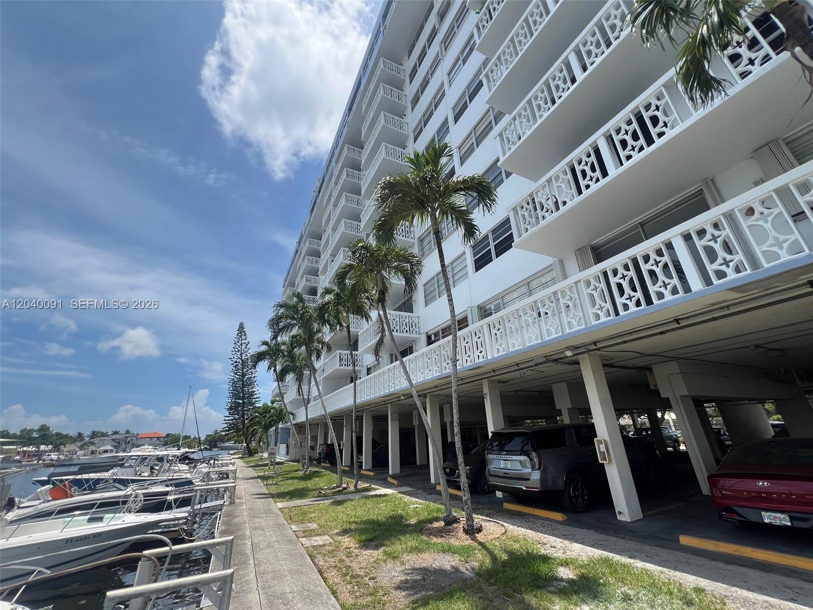 A multi-story residential building features balconies with decorative railings and ground-level covered parking spaces — 13155 Ixora Ct # 703, North Miami FL 33181, NORTH MIAMI, FL