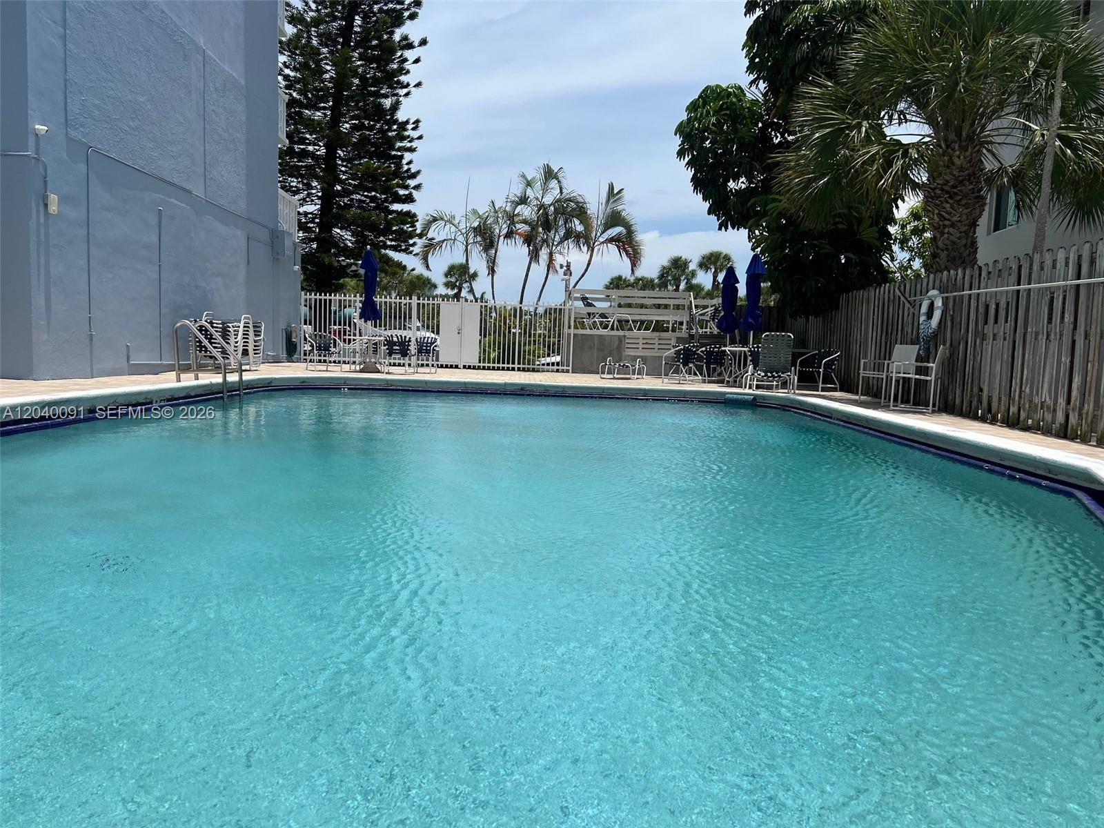 A swimming pool is surrounded by a patio, lounge chairs, and a wooden fence — 13155 Ixora Ct # 703, North Miami FL 33181, NORTH MIAMI, FL