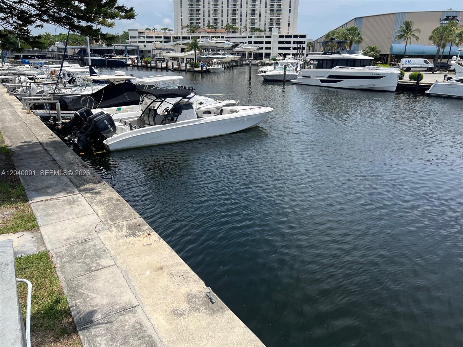 A marina features several docked motorboats along a concrete seawall with buildings in the background — 13155 Ixora Ct # 703, North Miami FL 33181, NORTH MIAMI, FL