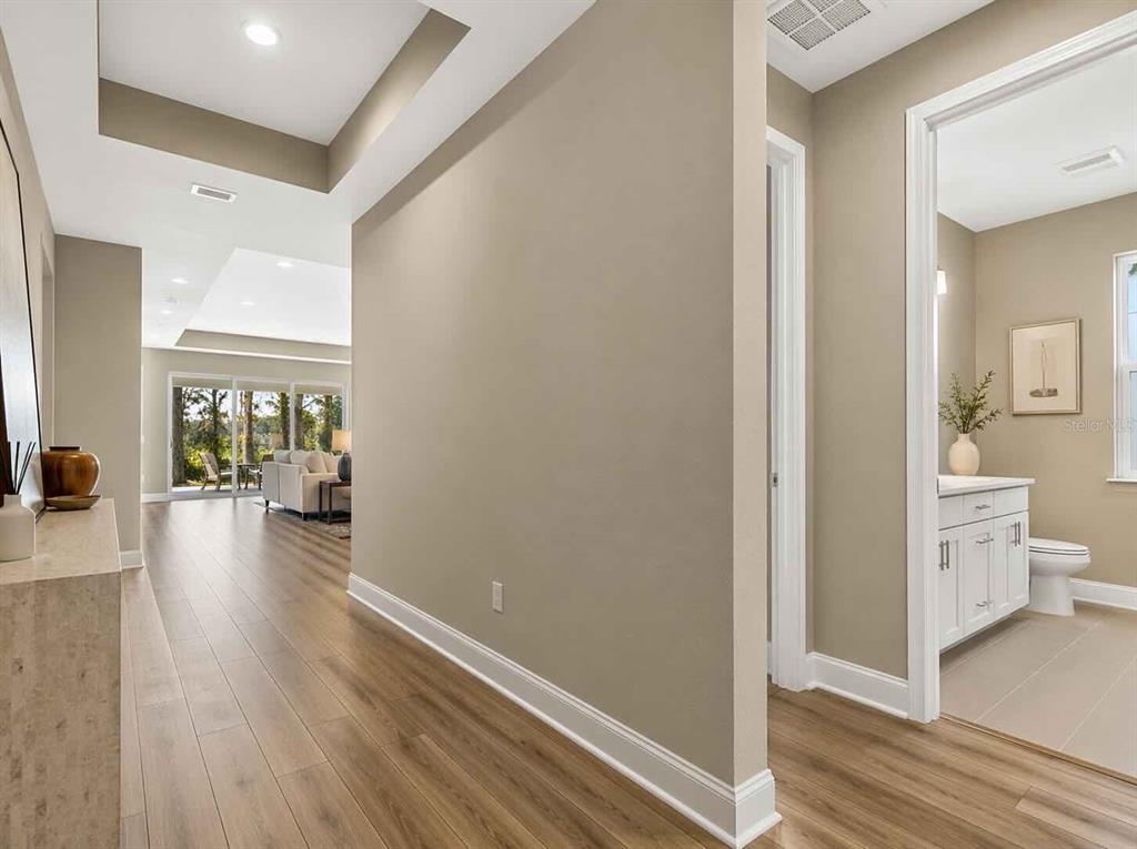 A hallway with light wood flooring leads to a living area and a bathroom — 3557 SECLUDED COURT, SARASOTA, FL