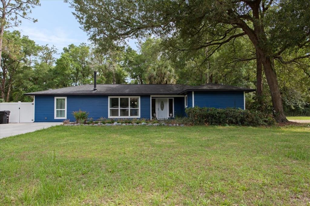 A single-story blue house with a white front door sits on a grassy lot — 10803 SW 92ND PLACE, GAINESVILLE, FL