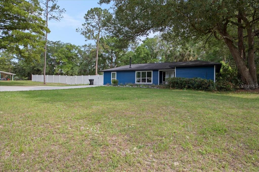 A blue, single-story house with a white fence sits on a large, grassy lot — 10803 SW 92ND PLACE, GAINESVILLE, FL