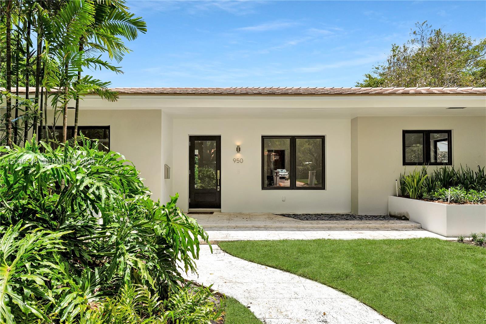 The exterior of a modern, single-story house features a white facade, black-framed windows, and landscaping — 950 Bayamo Ave, Coral Gables FL 33146, CORAL GABLES, FL
