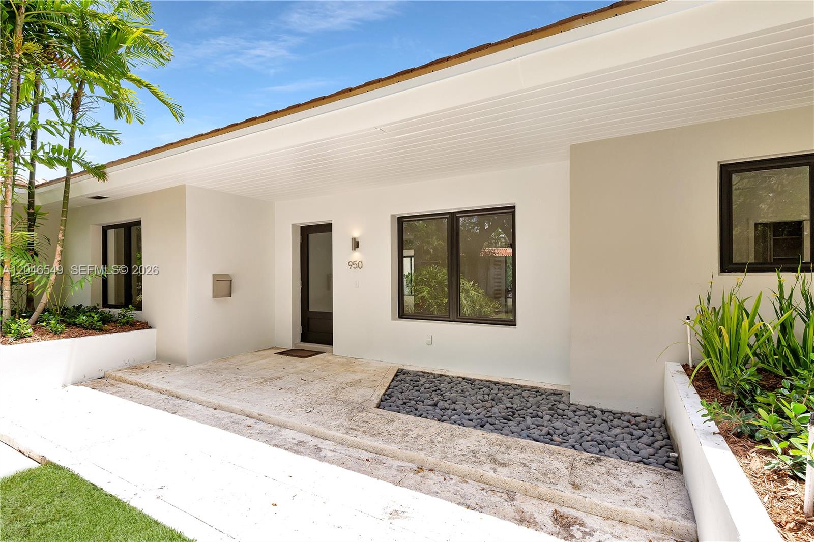 The exterior of a modern home features a white facade, dark window frames, and landscaping — 950 Bayamo Ave, Coral Gables FL 33146, CORAL GABLES, FL