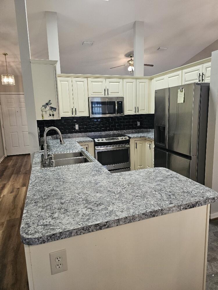 A kitchen features cream cabinets, granite countertops, a black subway tile backsplash, and stainless appliances — 1120 Fairfield Lane, Sebastian FL 32958, SEBASTIAN, FL