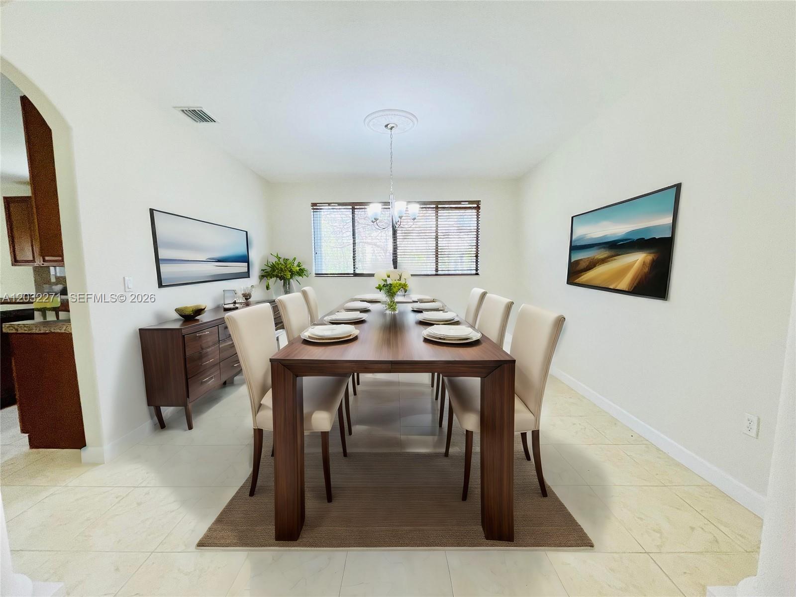 A dining room features a long wooden table, eight cream chairs, and two landscape paintings — 7427 SW 189th St, Cutler Bay FL 33157, CUTLER BAY, FL