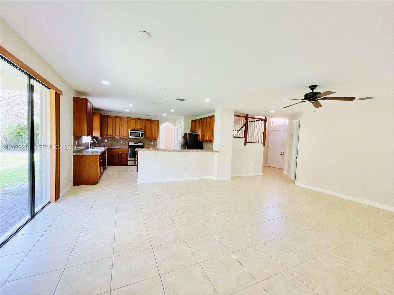 An open-concept kitchen with wood cabinets and tile flooring overlooks a spacious living area — 7427 SW 189th St, Cutler Bay FL 33157, CUTLER BAY, FL