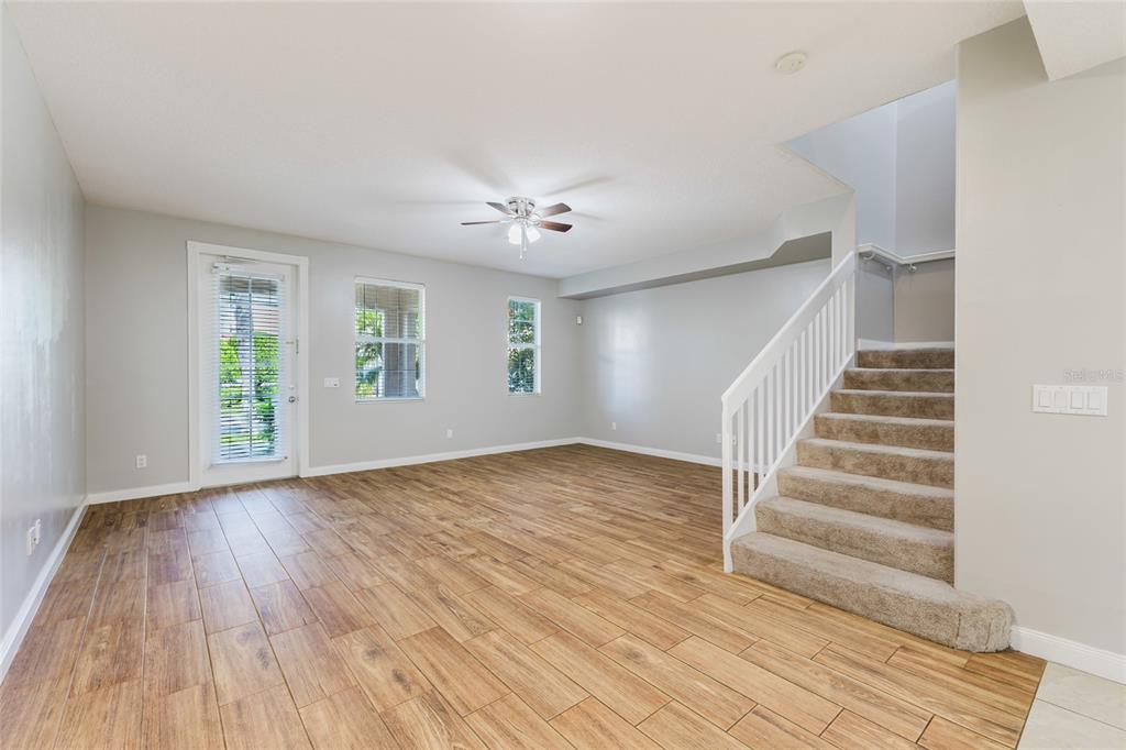 An empty living room features wood-look tile flooring, a ceiling fan, and carpeted stairs — 1648 NAPOLI DRIVE W, SARASOTA, FL