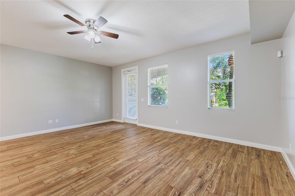 An empty room features light gray walls, wood-look tile flooring, a ceiling fan, and windows — 1648 NAPOLI DRIVE W, SARASOTA, FL
