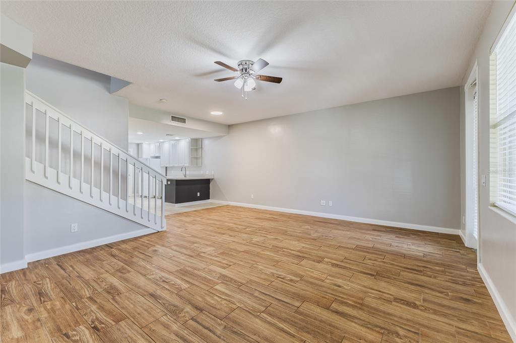 An open-concept living room features wood-look tile flooring, a ceiling fan, and a staircase — 1648 NAPOLI DRIVE W, SARASOTA, FL