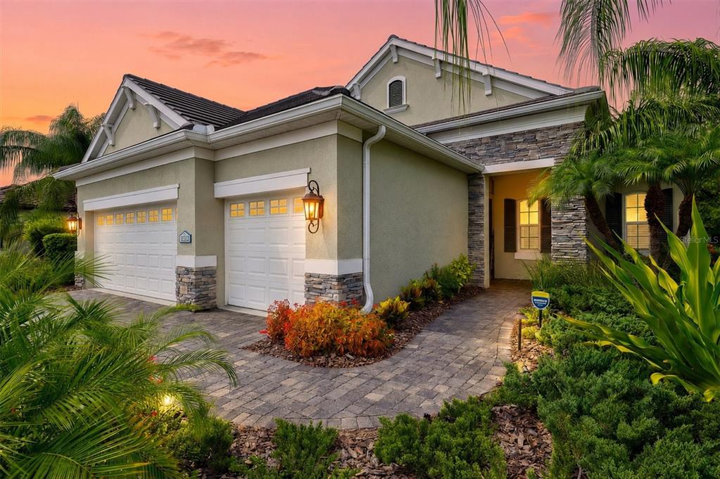 A single-story house with a two-car garage, stone accents, and a paved walkway at sunset — 21221 WACISSA DRIVE, VENICE, FL