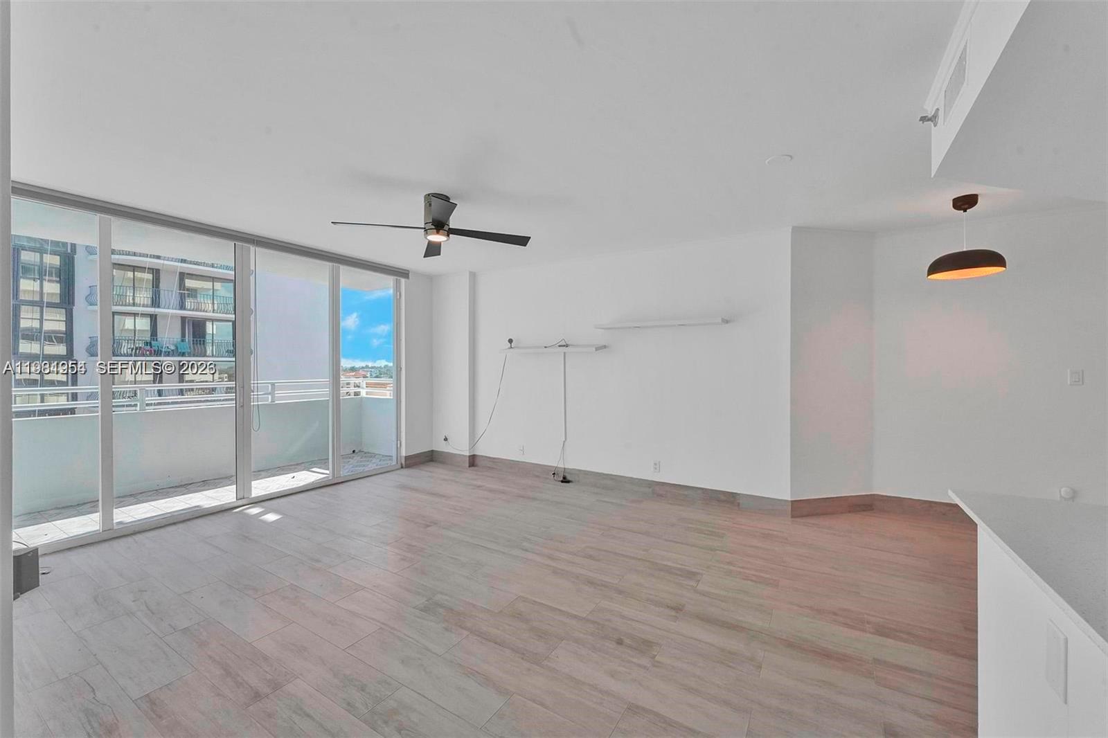 An empty living room features light wood-look tile floors, a ceiling fan, and sliding glass doors — 8911 Collins Ave # 703, Surfside FL 33154, SURFSIDE, FL