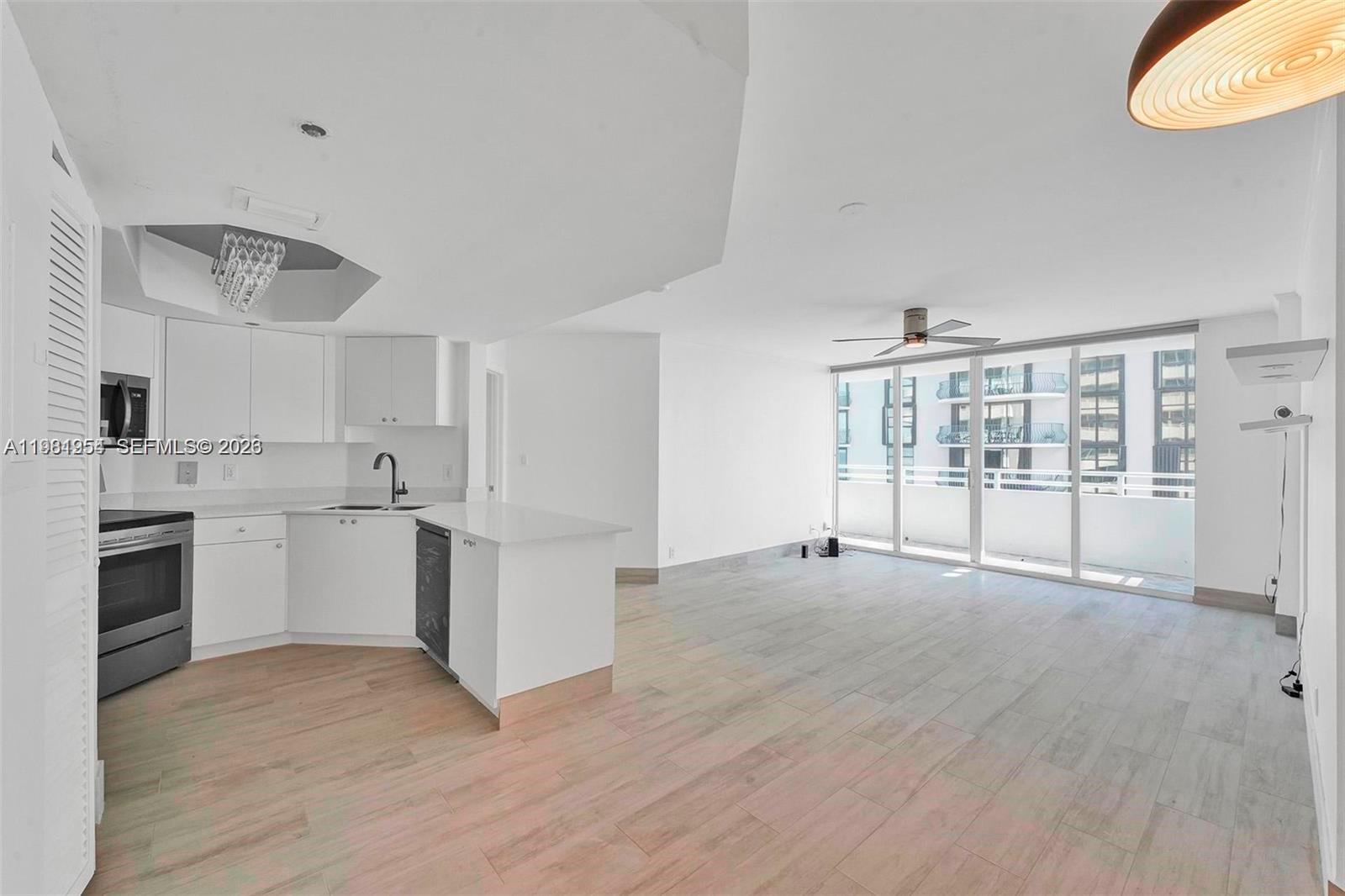 A kitchen with white cabinets and a peninsula opens into a bright living area — 8911 Collins Ave # 703, Surfside FL 33154, SURFSIDE, FL