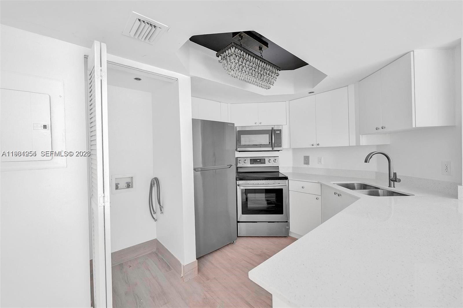 A kitchen features white cabinets, stainless steel appliances, and a crystal chandelier in a recessed ceiling — 8911 Collins Ave # 703, Surfside FL 33154, SURFSIDE, FL