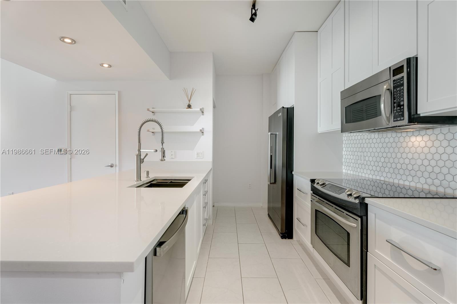 A modern kitchen features white cabinetry, quartz countertops, stainless steel appliances, and a tiled backsplash — 951 Brickell Ave # 3607, Miami FL 33131, MIAMI, FL